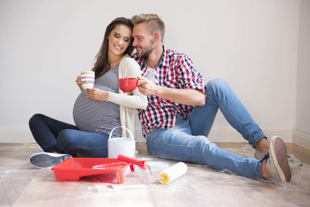 young couple sitting on floor of new home enjoying coffee taking a break from painting the room